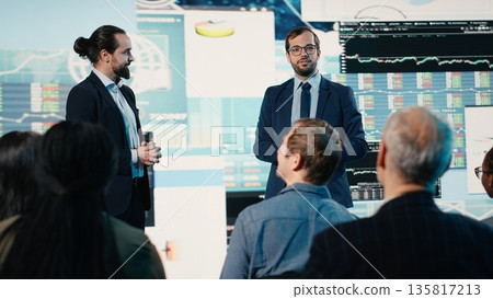 Two professional men delivering conference speech for diverse group audience. International business event in conference hall features professionals, networking and leadership discussion. 135817213