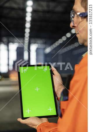 Vertical green screen tablet with inspector checking equipment in manufacturing plant, wearing safety vest for the engineering industrial operation behind heavy steel development. Vertical green screen tablet with inspector checking equipment in manufacturing plant, wearing safety vest for the engineering industrial operation behind heavy steel development. 135817215