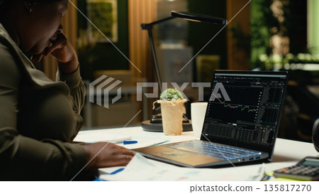 Black woman distressed about stock market trends going down and losing money, feeling scared and concerned about risk and bankruptcy. Studying forex data and being worried. Camera B. Black woman distressed about stock market trends going down and losing money, feeling scared and concerned about risk and bankruptcy. Studying forex data and being worried. Camera B. 135817270