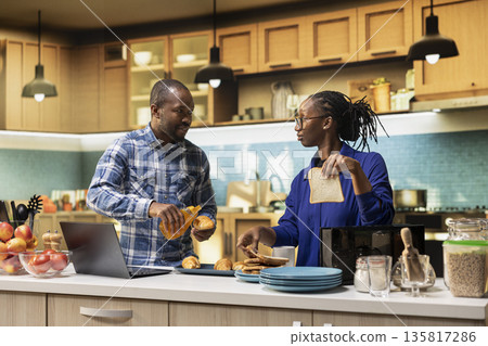 African American couple prepares croissants with honey and toast for delicious breakfast meal in the kitchen. Man and woman prepares homemade food, the joy of a healthy lifestyle. African American couple prepares croissants with honey and toast for delicious breakfast meal in the kitchen. Man and woman prepares homemade food, the joy of a healthy lifestyle. 135817286
