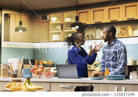 African American furious couple arguing in their kitchen at home. Woman appears angry while man looks upset and distraught, showing emotional tension and frustration in a difficult relationship. African American furious couple arguing in their kitchen at home. Woman appears angry while man looks upset and distraught, showing emotional tension and frustration in a difficult relationship. 135817294