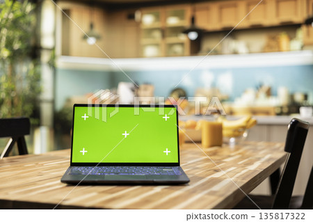 Green screen on laptop in the kitchen with rustic counter and elegant lighting. Cookware and utensils creating a comfortable and inviting household dining space with modern interior design. Green screen on laptop in the kitchen with rustic counter and elegant lighting. Cookware and utensils creating a comfortable and inviting household dining space with modern interior design. 135817322