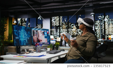 Black woman using VR glasses and neural networks to edit photos, retouching content and generating materials with machine learning and AI tools. Turning text to image with virtual reality. Camera A. Black woman using VR glasses and neural networks to edit photos, retouching content and generating materials with machine learning and AI tools. Turning text to image with virtual reality. Camera A. 135817323