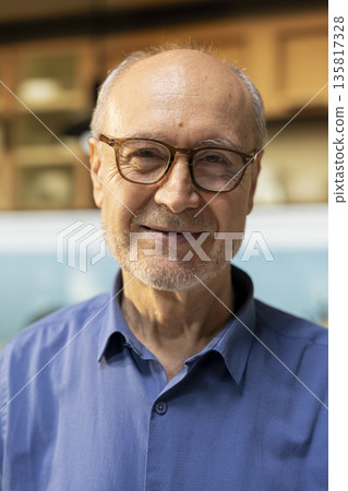 Portrait of senior adult standing at the kitchen counter with authentic smile, showing natural satisfaction in retired life. Peaceful morning routine and lifestyle enjoyment in his apartment. Portrait of senior adult standing at the kitchen counter with authentic smile, showing natural satisfaction in retired life. Peaceful morning routine and lifestyle enjoyment in his apartment. 135817328