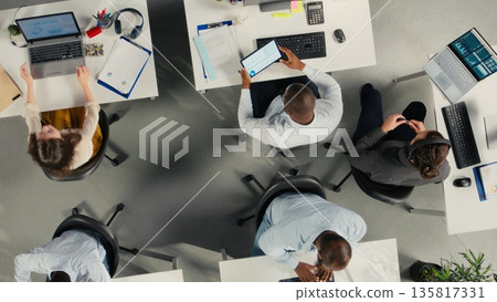 Top down view of employees engaged in business intel and analytics using data diagrams in office, staff reviews projections and reports to improve overall company strategy. Top down view of employees engaged in business intel and analytics using data diagrams in office, staff reviews projections and reports to improve overall company strategy. 135817331