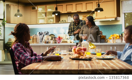 Parents and children at home serving breakfast in the kitchen, mother preparing the meal at the kitchen counter. Family moment captures warmth, morning joy and being together. Camera B. Parents and children at home serving breakfast in the kitchen, mother preparing the meal at the kitchen counter. Family moment captures warmth, morning joy and being together. Camera B. 135817368