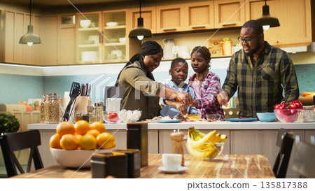 Parents and children sprinkling mozzarella and grated cheese on homemade pizza dough, laughing in the kitchen together in this family moment filled with joy and culinary creativity. Camera A. Parents and children sprinkling mozzarella and grated cheese on homemade pizza dough, laughing in the kitchen together in this family moment filled with joy and culinary creativity. Camera A. 135817388