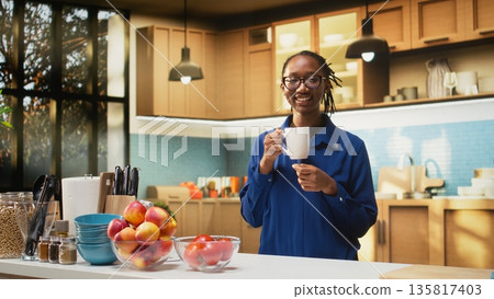 Happy adult in the kitchen smelling the fresh aroma of roasted coffee, serving delicious homemade breakfast. Woman uses prepare slices of toast with croissants and enjoys warm coffee cup. Happy adult in the kitchen smelling the fresh aroma of roasted coffee, serving delicious homemade breakfast. Woman uses prepare slices of toast with croissants and enjoys warm coffee cup. 135817403