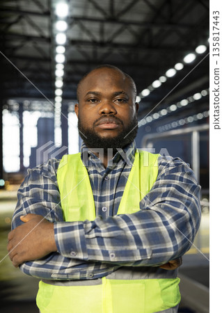 African american plant engineer standing near steel machinery during construction tasks, showcasing production responsibility and the power of fabrication. Hi vis vest for safety at work. 135817443