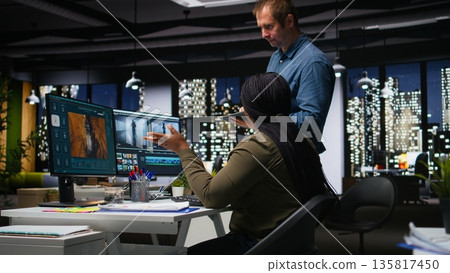 Diverse colleagues working together on video editing for a montage on software, digital media creation. Filmmaker and assistant using dual monitors to edit footage for web content. Camera A. Diverse colleagues working together on video editing for a montage on software, digital media creation. Filmmaker and assistant using dual monitors to edit footage for web content. Camera A. 135817450