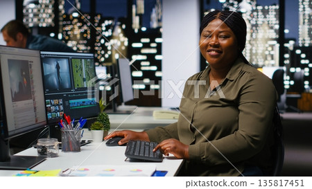 Female expert editor working in video production industry at agency office, doing color grading and creating a montage on dual monitors. Creative process with multimedia tech tools. Camera B. Female expert editor working in video production industry at agency office, doing color grading and creating a montage on dual monitors. Creative process with multimedia tech tools. Camera B. 135817451