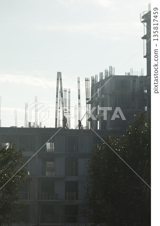 Tradesmen install steel framework on unfinished concrete skyscraper building during sunny day. Apartment complex being built by construction company crew members to accommodate population growth Tradesmen install steel framework on unfinished concrete skyscraper building during sunny day. Apartment complex being built by construction company crew members to accommodate population growth 135817459
