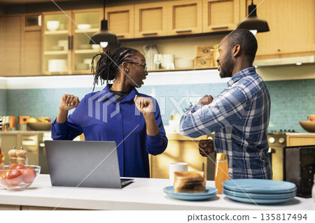 Happy african american couple dancing together in a cozy kitchen, moving with rhythm and morning music. Relaxed man and woman sharing laughter and positive energy in the morning. Happy african american couple dancing together in a cozy kitchen, moving with rhythm and morning music. Relaxed man and woman sharing laughter and positive energy in the morning. 135817494