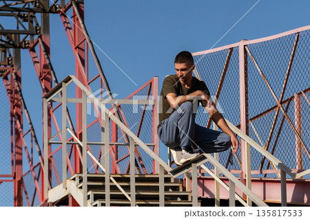 Man crouches on stair handrail in urban parkour structure Man crouches on stair handrail in urban parkour structure 135817533