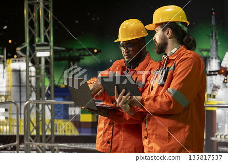Offshore platform crew members using laptop to analyze extraction efficiency during aurora borealis. Engineers on drilling rig deck configuring vessel management systems under green arctic lights Offshore platform crew members using laptop to analyze extraction efficiency during aurora borealis. Engineers on drilling rig deck configuring vessel management systems under green arctic lights 135817537