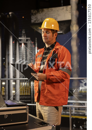 Industrial worker assesses natural gas extraction data on oil drilling platform, ensuring efficient petroleum extraction within the oil and gas industry. Environmental officer at the refinery. 135817550