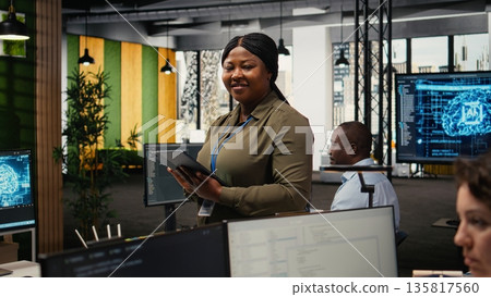 Portrait of smiling engineer working in office, using specialized hardware to accelerate complex AI calculations. Happy woman managing systems for machine learning training datasets, camera A 135817560