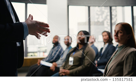 Business summit in conference hall with professional audience seated on chairs. Speaker delivers presentation during panel discussion, encouraging engagement and discussion among attendees. Business summit in conference hall with professional audience seated on chairs. Speaker delivers presentation during panel discussion, encouraging engagement and discussion among attendees. 135817581