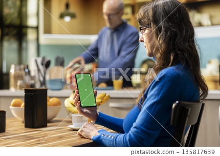 Green screen on mobile phone with pensioner at the breakfast table, retirement lifestyle with healthy food and coffee for cozy atmosphere at home. Senior man checking display. 135817639