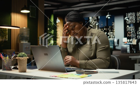 Female entrepreneur sighing being drained and overwhelmed after hours, pushing limits despite clear signs of fatigue and tension. Workplace challenges and discouragement bring discomfort. Camera A. 135817643