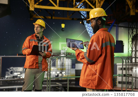 African american worker performing inspection and emission tracking on offshore drilling rig under aurora borealis, compliance with natural gas and petroleum extraction rules. 135817708