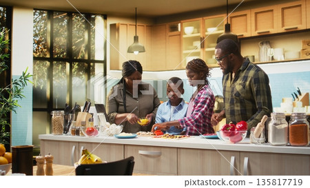 African American cute family laughing while preparing homemade pizza in the kitchen. Enjoying family bonding time, teamwork and the joy of home cooking during the weekend. Camera A. African American cute family laughing while preparing homemade pizza in the kitchen. Enjoying family bonding time, teamwork and the joy of home cooking during the weekend. Camera A. 135817719