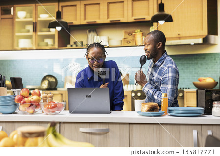 Overjoyed African American couple singing karaoke in the kitchen, showing positive energy and entertainment. People shows affectionate bond and creates a fun groovy atmosphere. Overjoyed African American couple singing karaoke in the kitchen, showing positive energy and entertainment. People shows affectionate bond and creates a fun groovy atmosphere. 135817771