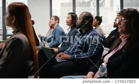 Black businessman takes notes on laptop at professional summit, forum conference with panel discussion and public speaker. Multiracial audience listen to ideas for entrepreneurship. 135817803