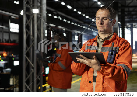 Professional employee in a warehouse uses tablet gear to guide operator teams through assembly tasks, demonstrating engineering and consistent manufacturing process activity. Automation. Professional employee in a warehouse uses tablet gear to guide operator teams through assembly tasks, demonstrating engineering and consistent manufacturing process activity. Automation. 135817836