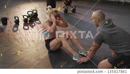 Woman in athletic wear doing sit-ups on gym mat, with coach support, kettlebells and punching bag 135817861