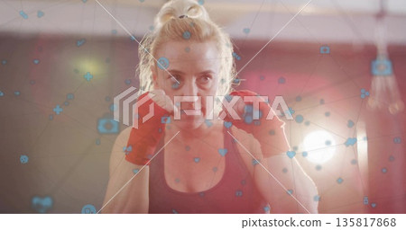 Standing boxer holding fists in boxing gym, with dark tank top, red wraps, network icons Standing boxer holding fists in boxing gym, with dark tank top, red wraps, network icons 135817868