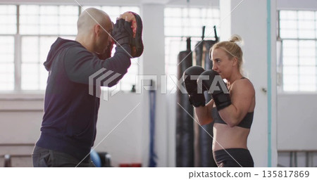 Exchanging jabs trainee and trainer sparring in gym, with focus mitts, boxing gloves, punching bags 135817869
