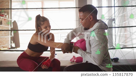 Male trainer in hoodie adjusting trainee's pink boxing gloves in gym boxing ring, punching bag Male trainer in hoodie adjusting trainee's pink boxing gloves in gym boxing ring, punching bag 135817870