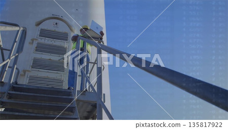Holding open laptop, construction worker in hard hat comparing data on tower platform with railing 135817922