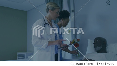 Doctor in white coat holding tablet and nurse arranging flowers beside patient in hospital room Doctor in white coat holding tablet and nurse arranging flowers beside patient in hospital room 135817949