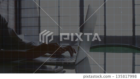 Typing woman in long-sleeved top at office desk by window, with laptop and smartphone reflecting 135817998