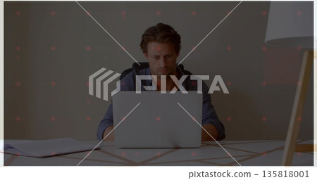 Man in button-down shirt typing on laptop in home office, with papers, patterned table, floor lamp Man in button-down shirt typing on laptop in home office, with papers, patterned table, floor lamp 135818001