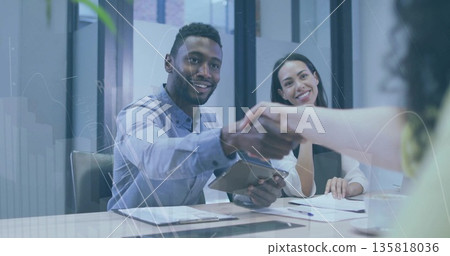 Shaking hands businessman reaching across glass table in meeting room, with tablet and documents Shaking hands businessman reaching across glass table in meeting room, with tablet and documents 135818036