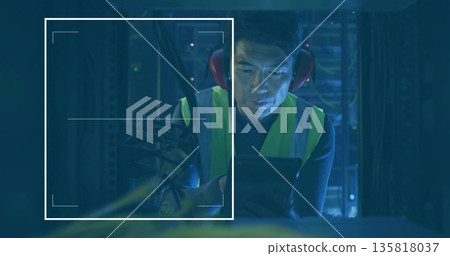 Kneeling Korean technician inspecting tablet in data center, with LEDs server racks safety vest 135818037
