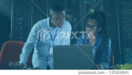 Two IT professionals troubleshooting network equipment in data center, with laptop, server racks Two IT professionals troubleshooting network equipment in data center, with laptop, server racks 135818041