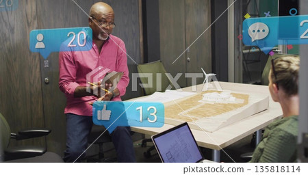 Presenting architect wearing pink shirt and jeans at conference table, with scale model, tablet Presenting architect wearing pink shirt and jeans at conference table, with scale model, tablet 135818114