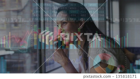 Smiling woman wearing blazer holding smartphone to ear at office window, with financial charts Smiling woman wearing blazer holding smartphone to ear at office window, with financial charts 135818171