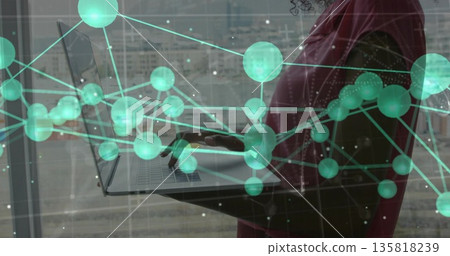 Woman wearing red blazer typing on laptop with network overlay in office by window, copy space Woman wearing red blazer typing on laptop with network overlay in office by window, copy space 135818239