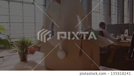 Packing items senior male office worker placing plant, lamp and headphones into box at wooden desk 135818241