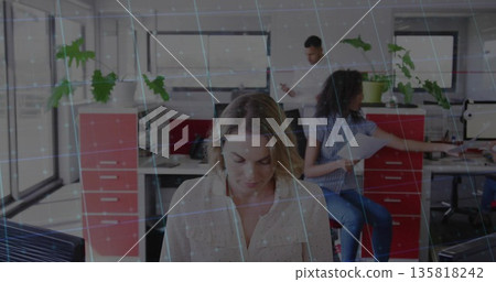 Reviewing printed document woman in light blouse sitting at desk in office, with computer monitors 135818242