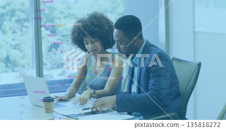 Collaborating colleagues in suits reviewing documents at conference table with laptop and pen Collaborating colleagues in suits reviewing documents at conference table with laptop and pen 135818272
