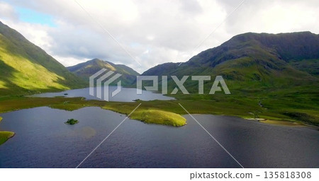 Showing narrow grassy peninsula extending into glacial valley lakes with islet and mountain slopes Showing narrow grassy peninsula extending into glacial valley lakes with islet and mountain slopes 135818308