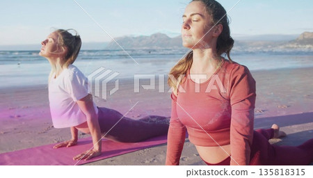 Practicing two women in sportswear holding cobra poses on sandy beach, with colorful yoga mats Practicing two women in sportswear holding cobra poses on sandy beach, with colorful yoga mats 135818315