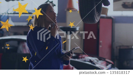 Inspecting female auto technician analyzing underside holding tablet in garage, with vehicle hoist Inspecting female auto technician analyzing underside holding tablet in garage, with vehicle hoist 135818317