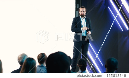 Male CEO presenting new mobile phone product launch on stage with premiere of modern smartphone interface. Entrepreneur introduces innovation and development with product release. 135818346